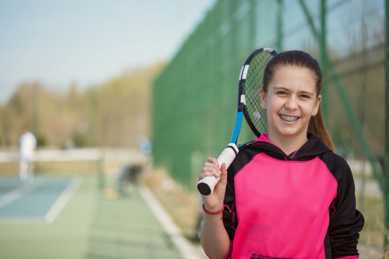 Girl wearing braces and carrying a tennis racquet.
