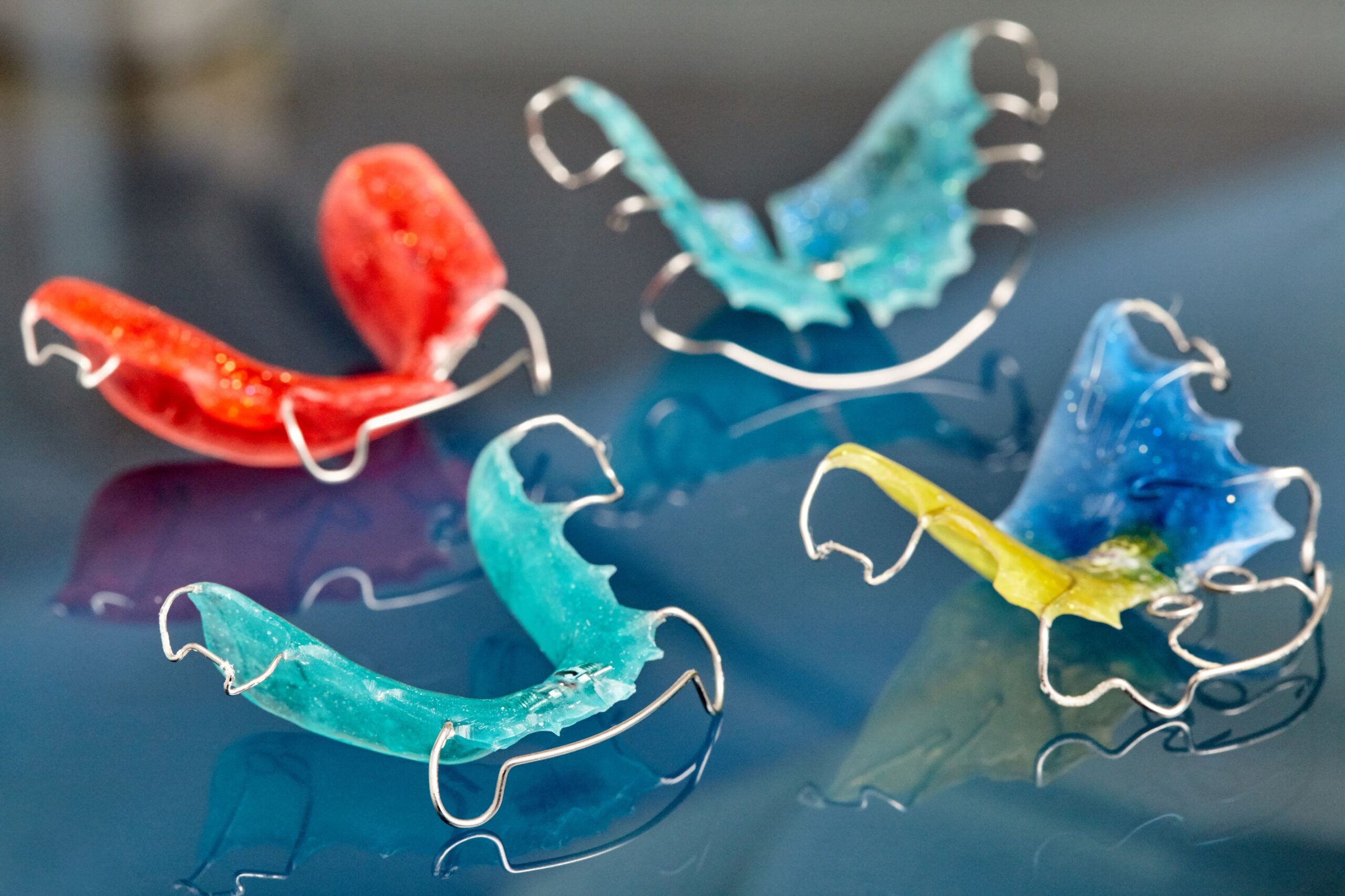 Four colorful retainers on a reflective surface.